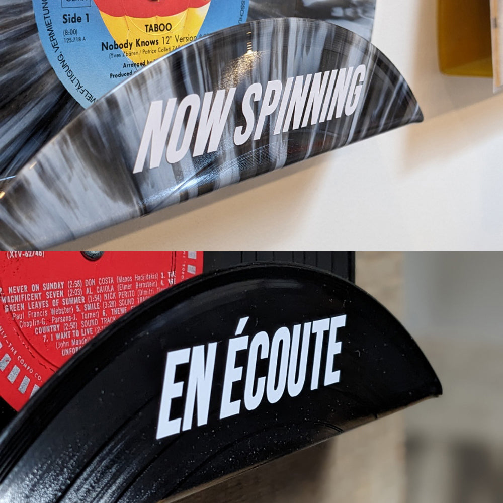 Image of a vinyl record display shelf with a sticker that reads 'Now Spinning' (En Écoute).